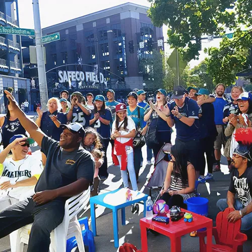 A crowd of excited Seattle Mariners fans gathered outdoors near Safeco Field on a sunny day.