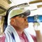 Man in a cap and sunglasses drinks from a blue bottle with a towel draped around his neck.