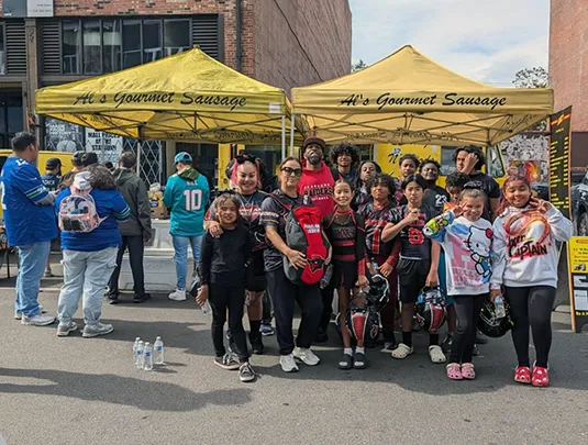 A youth football team poses together in front of yellow food tents at an outdoor event.