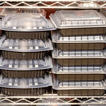 Stacks of black plastic takeout containers with clear lids on a metal wire shelf.