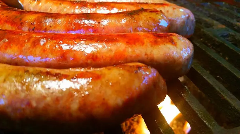 Four sausages are sizzling on a grill over an open flame, glistening with juices.