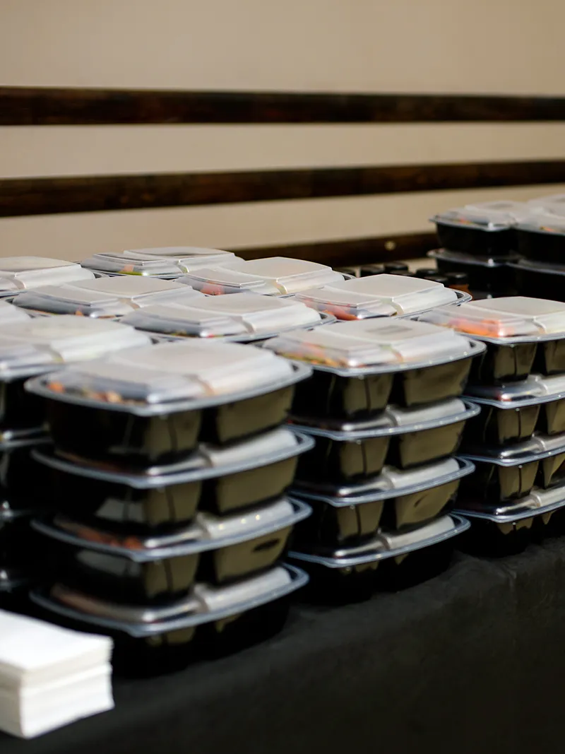 Stacks of black plastic meal prep containers with clear lids arranged on a table.