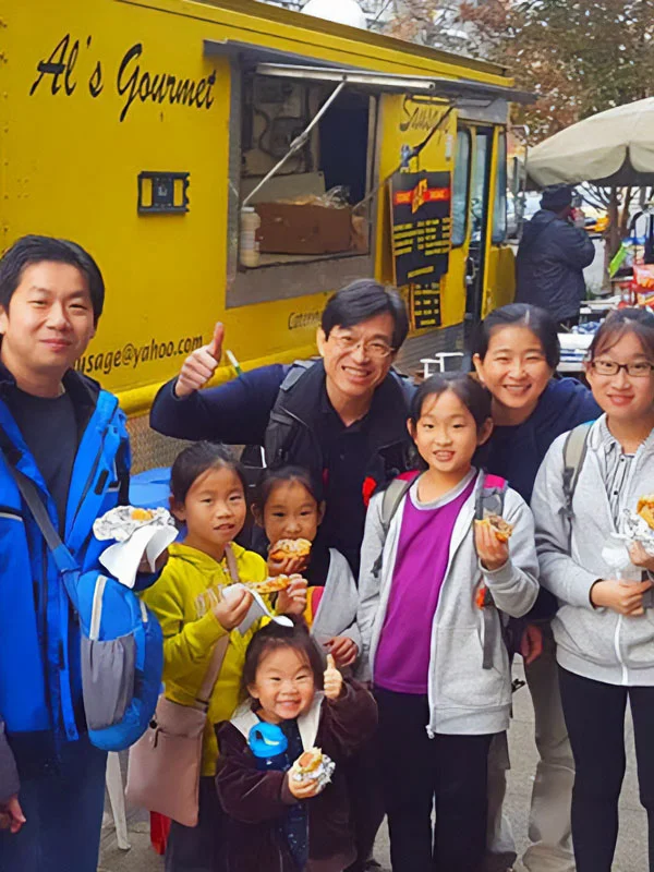 A smiling family stands in front of a yellow food truck, holding food and posing for a group photo.